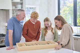 Family of four looking down over skittles board game as they play.