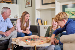 Mother, daughter, and son smiling as they play on a full size carrom board.