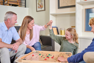 Mother and daughter high five as family plays on a full size carrom board.