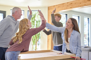 Parents and two children high five each other while playing four person nok hockey.