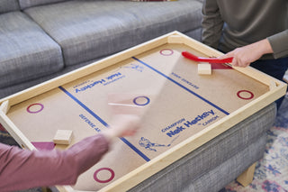 Hands moving quickly while playing on a small nok hockey game board.